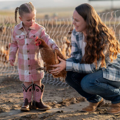 Mother holding a chicken for her daughter wearing Durango boots on a sunny farm day