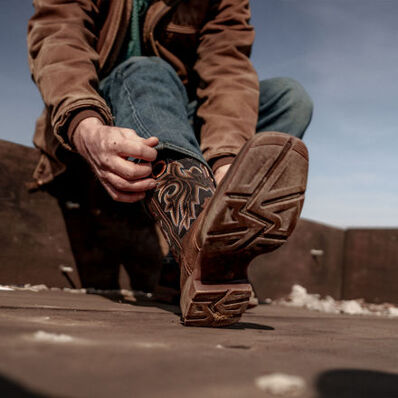 Man pulling on Rebel™ Durango western boots on the back of a pickup truck